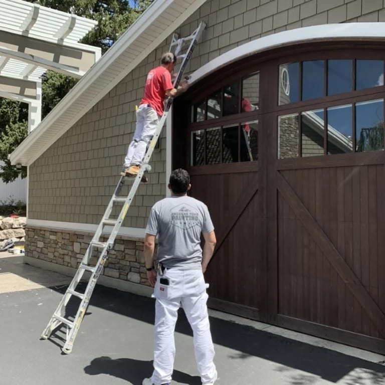 Two men from American Town Painting are painting a garage door in a residential setting.