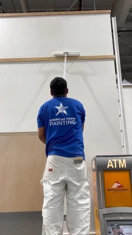 A man in a blue shirt paints a wall, showcasing his work for American Town Painting.