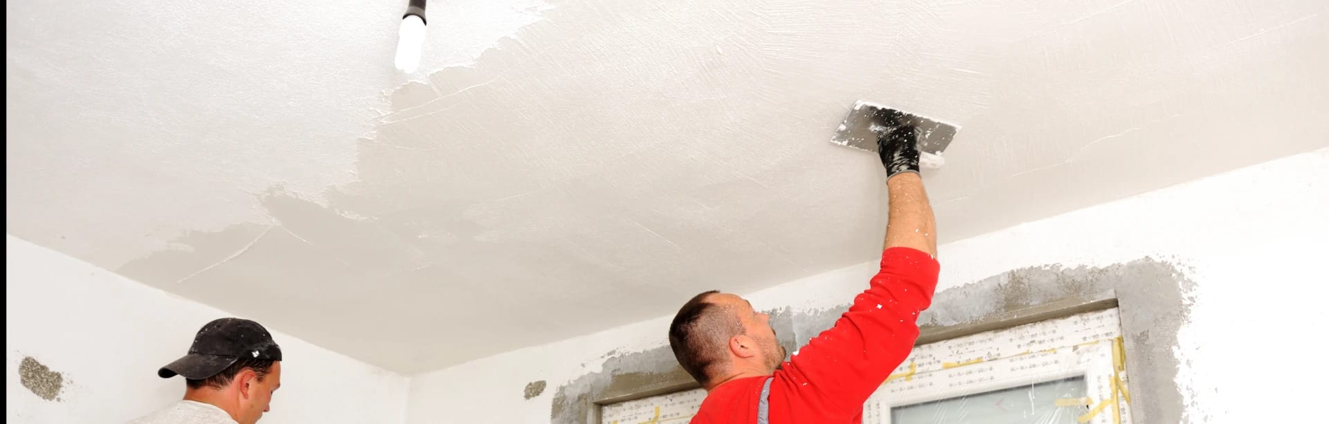 Two men from American Town Painting are painting the ceiling of a room with brushes and ladders.